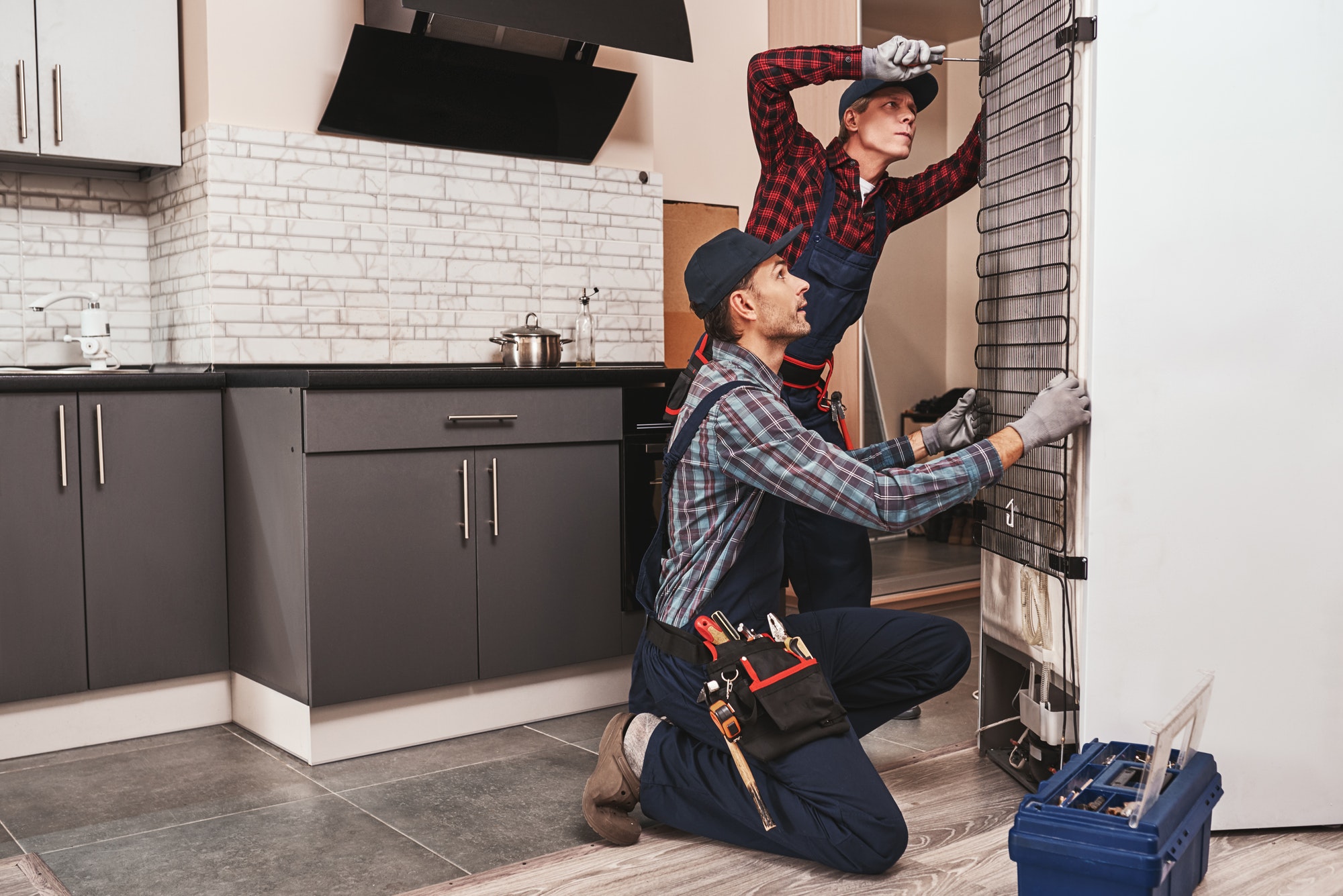 Two handymen with refrigerator. Young men mechanics checking refrigerator